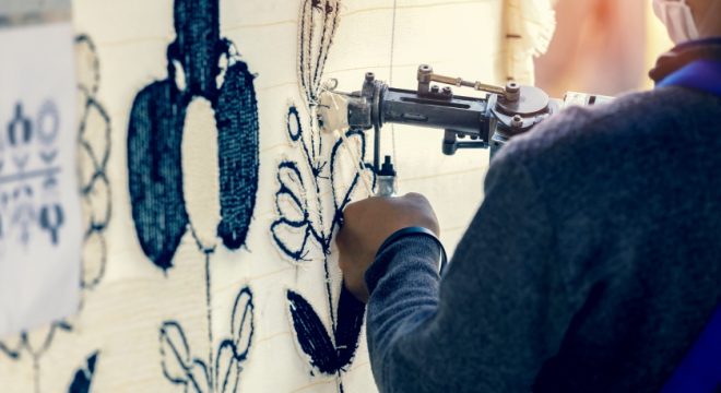 Side view of stand weaver holding tools still weaving carpet